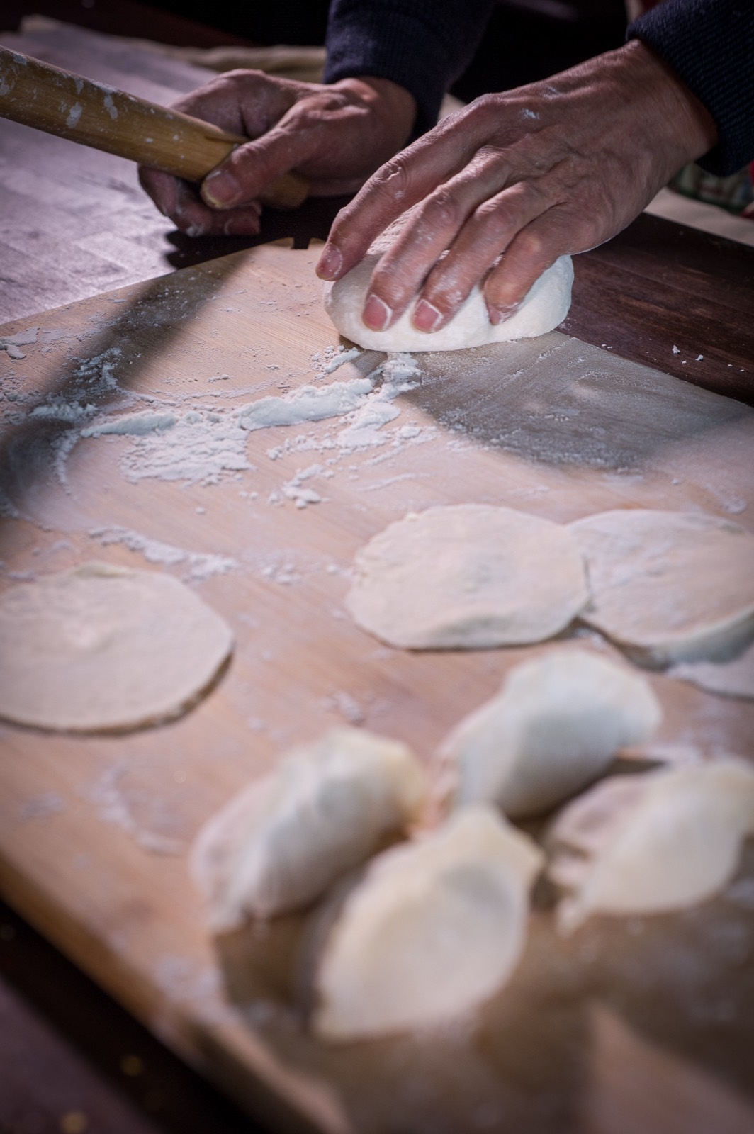 Hands rolling fresh dumpling wrappers by hand