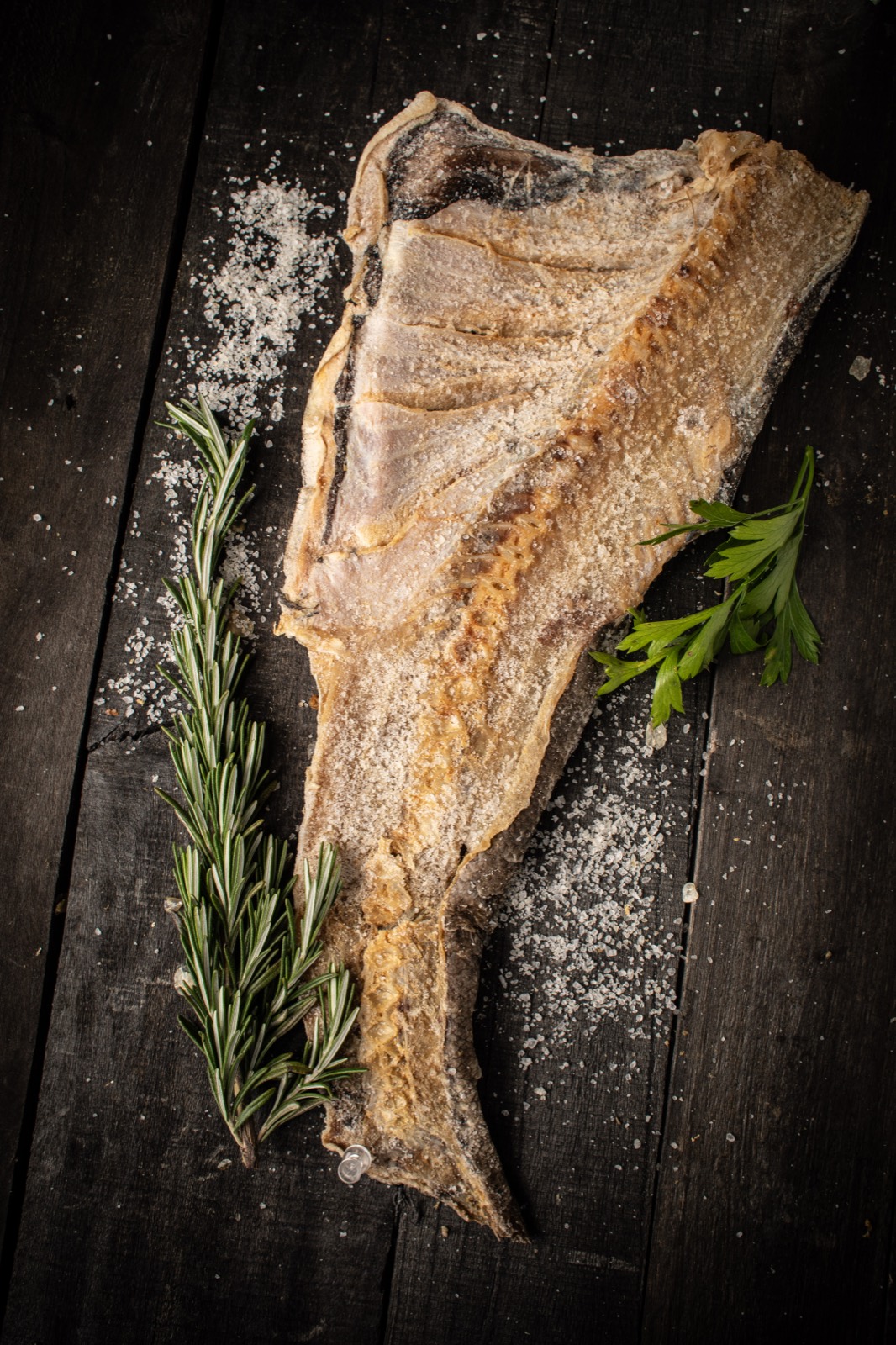Dried carp fillet with rosemary and sea salt on dark wood